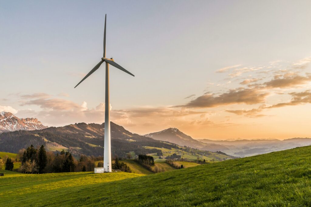 A wind turbine on a green hillside with mountains in the background during sunset.